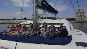 Personas sentadas en la proa del catamarán con la Torre de Belém al fondo