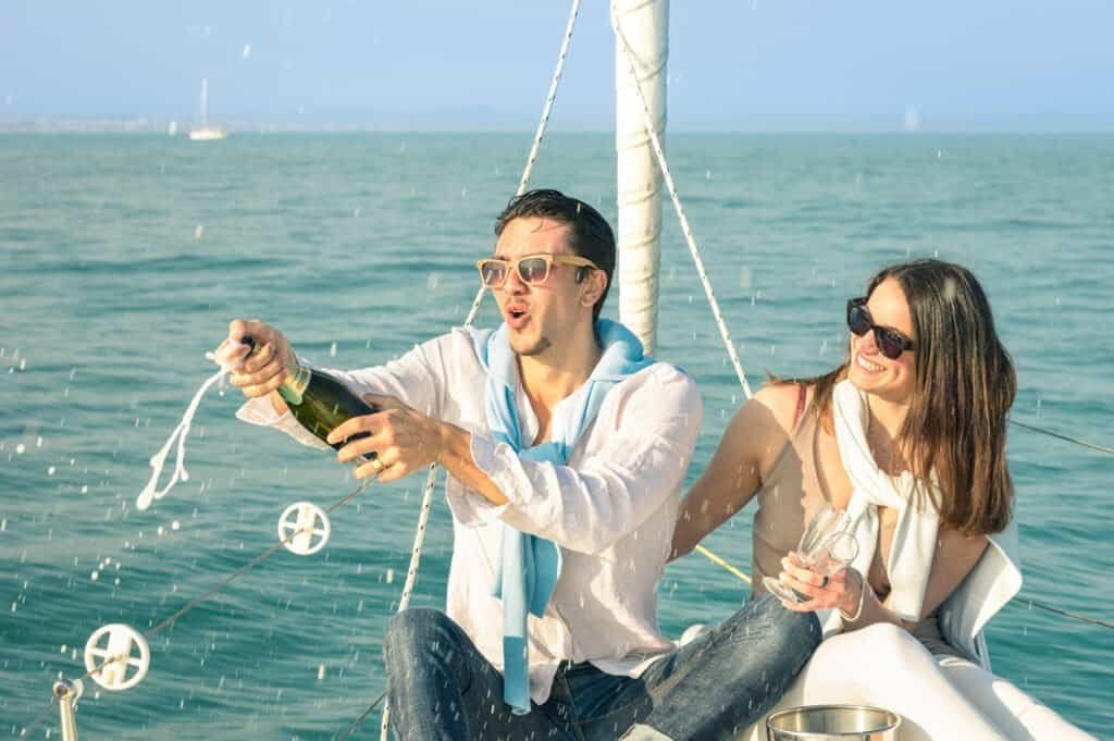 Pareja de jóvenes enamorados en un velero brindando con una botella de champán - Feliz fiesta de cumpleaños de novia en un crucero de lujo en velero