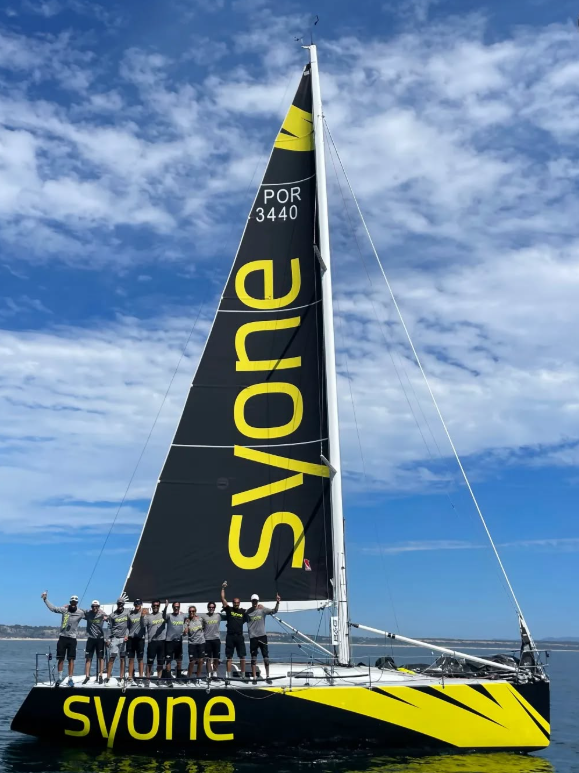 El barco del equipo Syone Sailing en plena acción, destacando la gran vela mayor con el logotipo de Syone