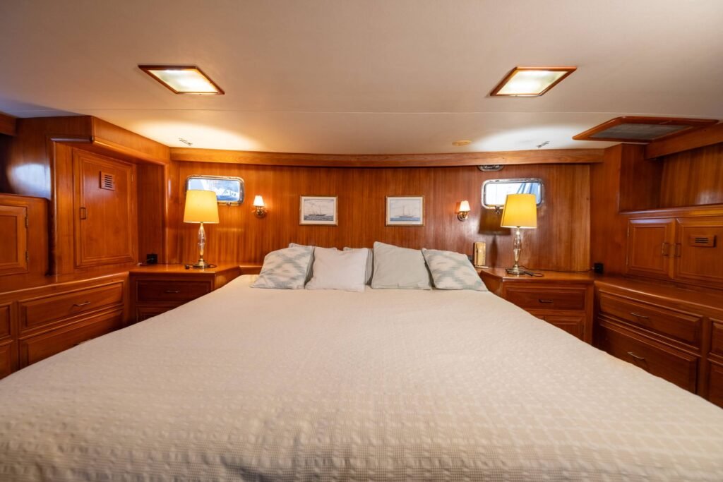 Cabine principal espaçosa e acolhedora no interior do Trawler Alexander 56, destacando a decoração clássica em madeira nobre e cama de casal confortável para longas viagens.