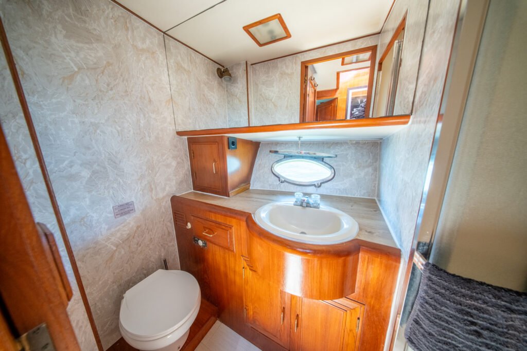 Casa de banho privativa a bordo do iate Alexander 56, equipada com lavatório, sanita, espelho e armários em madeira clássica com acabamento náutico.